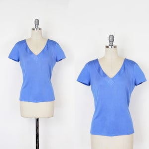 Könnte beinhalten: Zwei hellblaue V-Ausschnitt-T-Shirts, die auf Schaufensterpuppen präsentiert werden. Die Shirts haben kurze Ärmel und ein schlichtes, klassisches Design. Der Stoff ist einfarbig und glatt. Die Schaufensterpuppen stehen vor einem schlichten weißen Hintergrund.