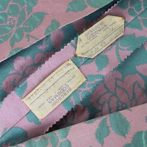 May include: Close-up of vintage fabric with a floral pattern in pink and teal. The fabric has a textured appearance. Two tags from Bergdorf Goodman, New York, are visible, with handwritten details including a date.