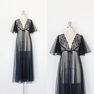 May include: A floor-length black sheer robe featuring a deep V-neckline adorned with intricate black lace trim. The garment includes flowing flutter sleeves and a delicate tie closure at the center of the chest, creating a layered appearance.
