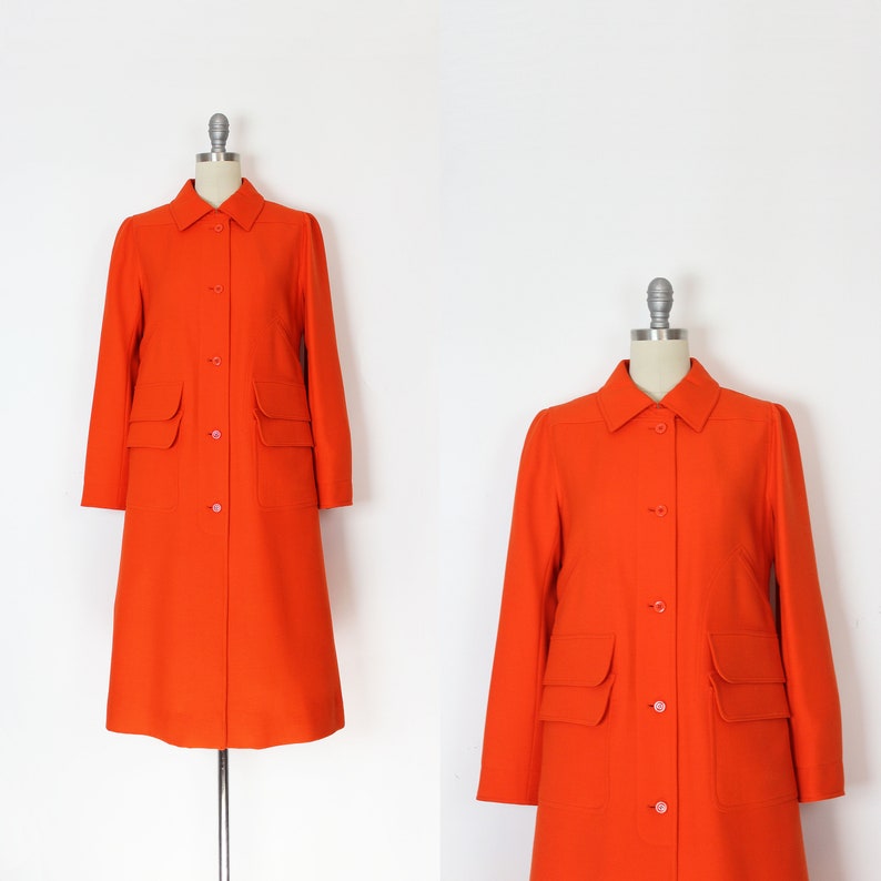 May include: A bright orange long-sleeved coat with a button-up front and two large pockets. The coat is on a mannequin.