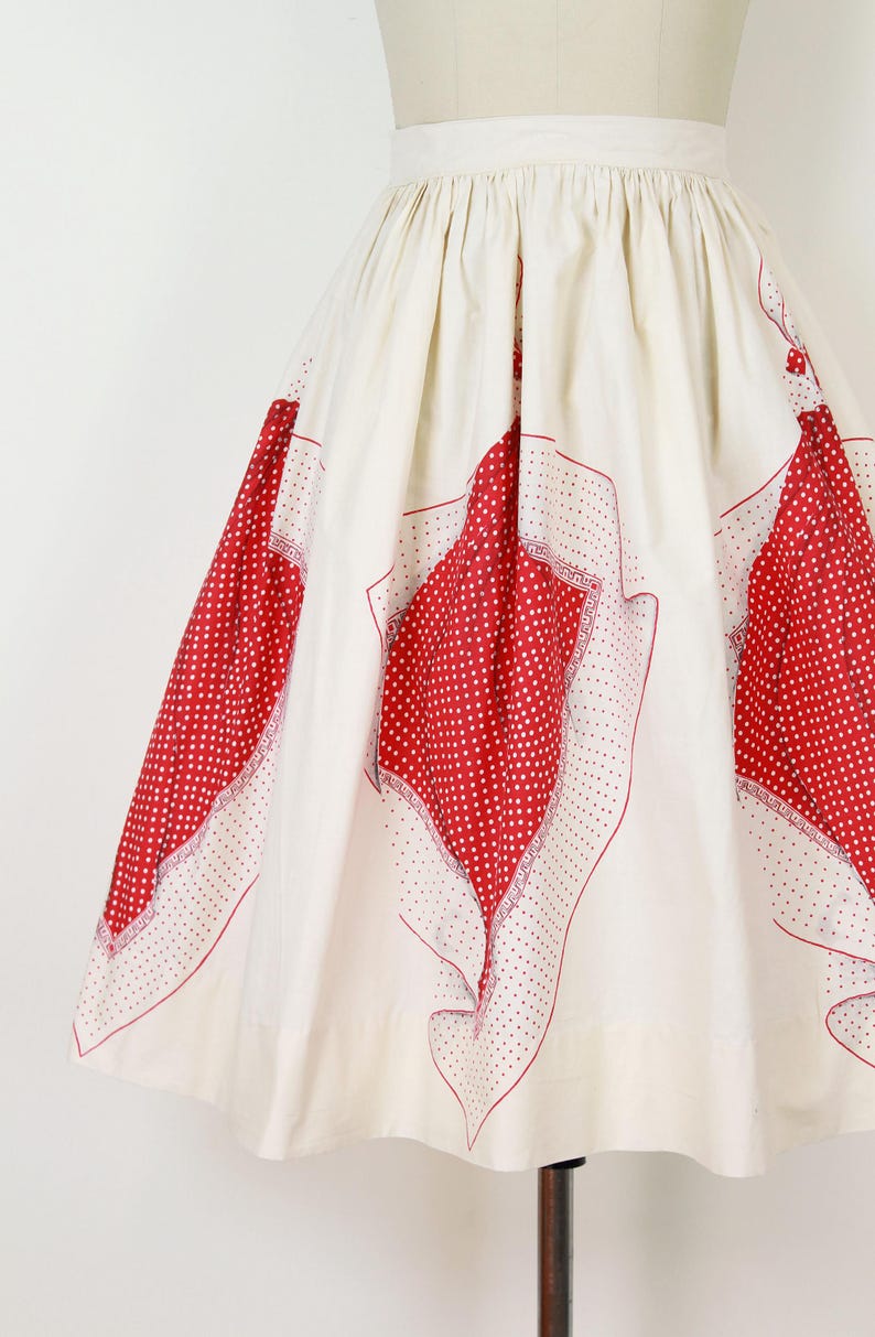 May include: A vintage-style skirt in cream fabric with large red polka dot patterns. The skirt features a high waist and a full, flowing silhouette. The red patterns are framed with a delicate white border.