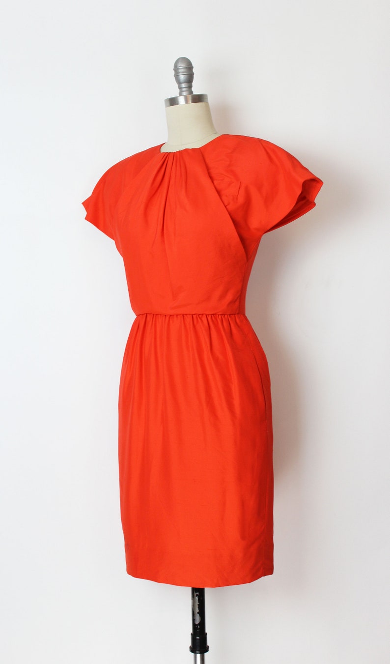 May include: A bright orange short-sleeved dress with a gathered neckline and a fitted silhouette.