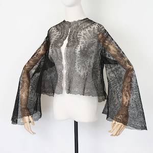 May include: Black lace jacket with flared sleeves, displayed on a mannequin. The jacket features an open front and intricate floral patterns. The sleeves extend to the wrists, showcasing a delicate design.