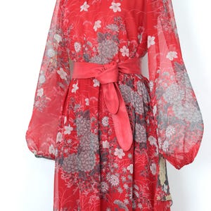 May include: A red maxi dress with a floral print and a matching red belt. The dress has long sleeves and a flowing skirt.