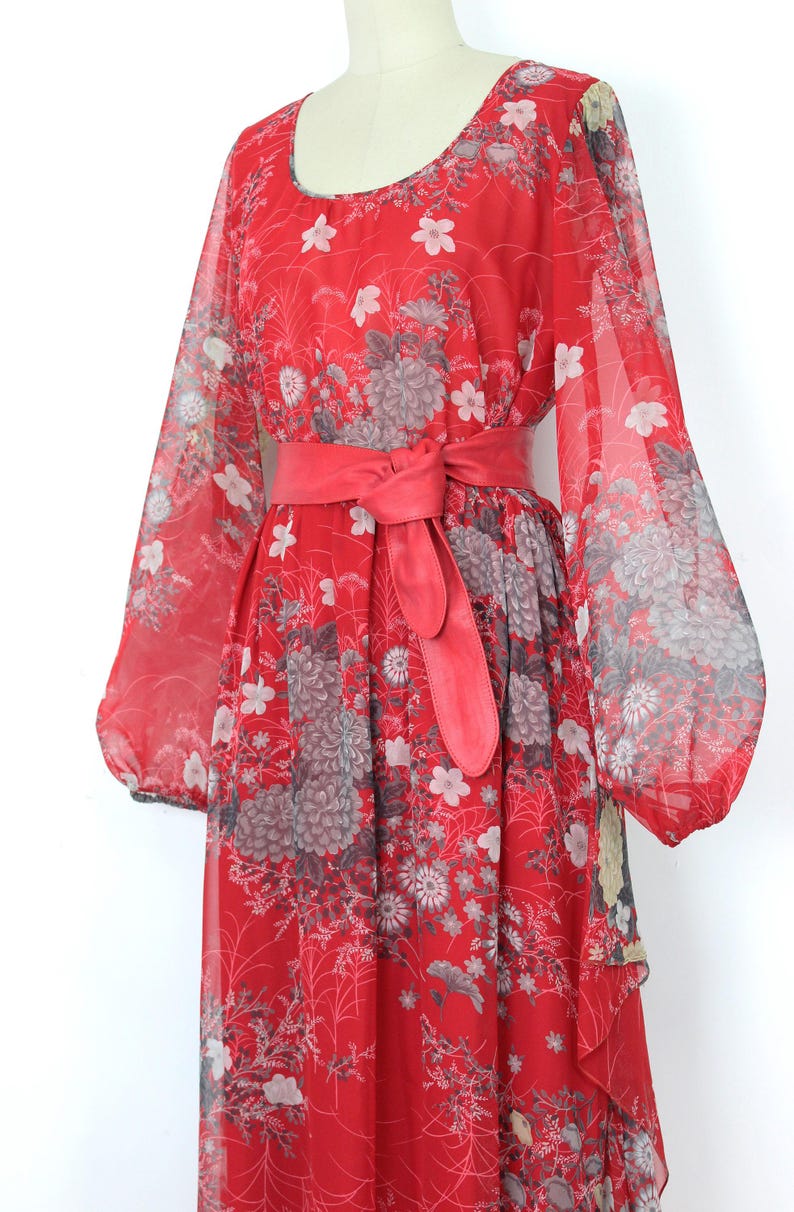 May include: A red maxi dress with a floral print and a matching red belt. The dress has long sleeves and a flowing skirt.