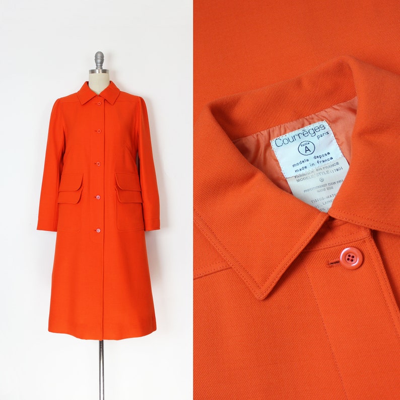 May include: A bright orange long-sleeved coat with a button-up front and two patch pockets. The coat has a label on the collar that reads "Courr&egrave;ges Paris" and "mod&egrave;le d&eacute;pos&eacute; made in France".