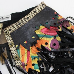 May include: A black leather vest with colorful, abstract painted accents and fringe. The vest features a decorative trim with gold-colored buttons and a beaded necklace. The label reads "SENTIMENTAL EXCLUSIVE DESIGN."