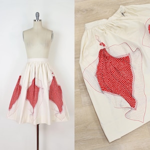 May include: Cream-colored skirt with red polka dot and solid red accents. The skirt features a high waist and a flared silhouette. The red accents are in a leaf-like shape and are outlined with red stitching. The skirt is displayed on a mannequin.