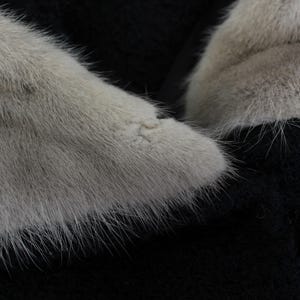 Puede incluir: Primer plano de una secci&oacute;n de una prenda de piel. La piel es de color gris claro con pelos largos y suaves. El fondo es negro, creando un contraste con la piel. La textura de la piel es visible.