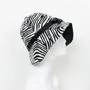 May include: A black and white zebra print bucket hat with a black grosgrain ribbon around the crown.