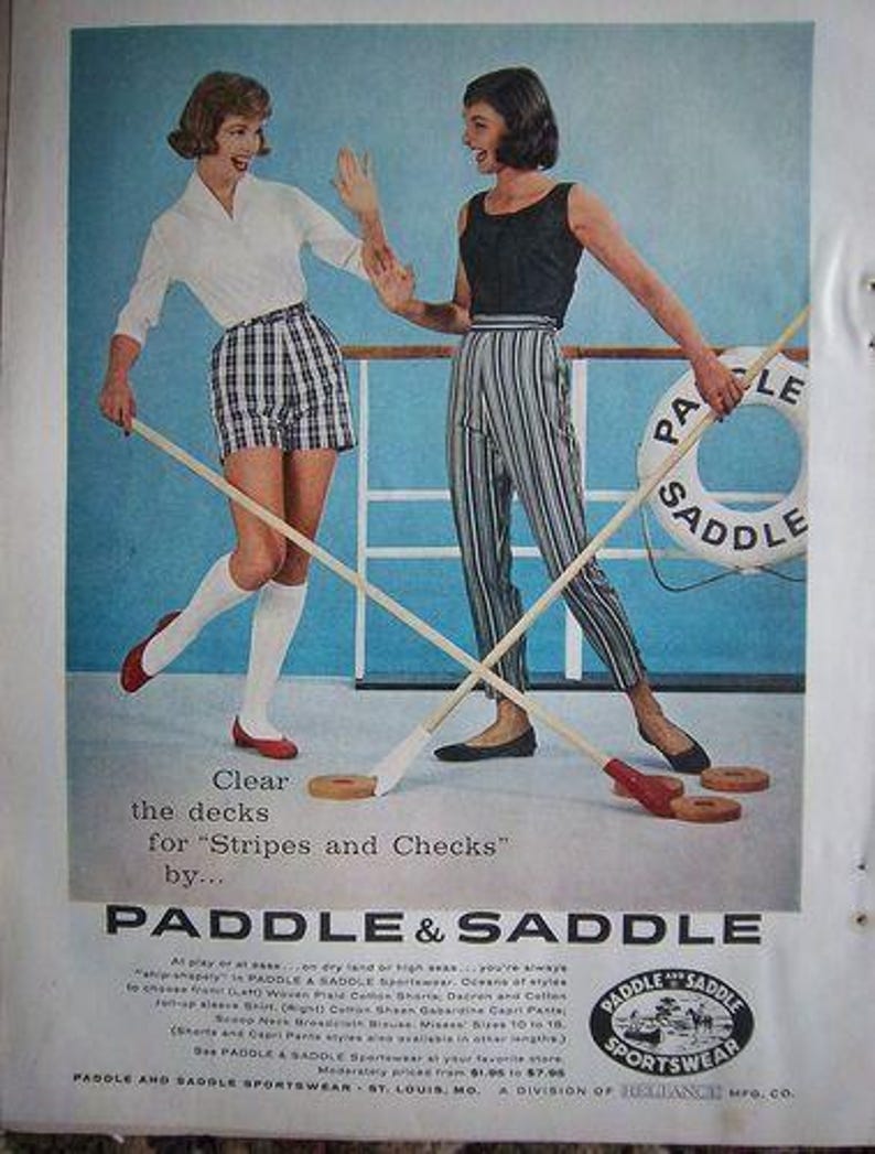 May include: Vintage advertisement featuring two women playing a game with wooden mallets and rings. One woman wears a white shirt and plaid shorts, the other a black top and striped pants. The text reads "Paddle & Saddle Sportswear."