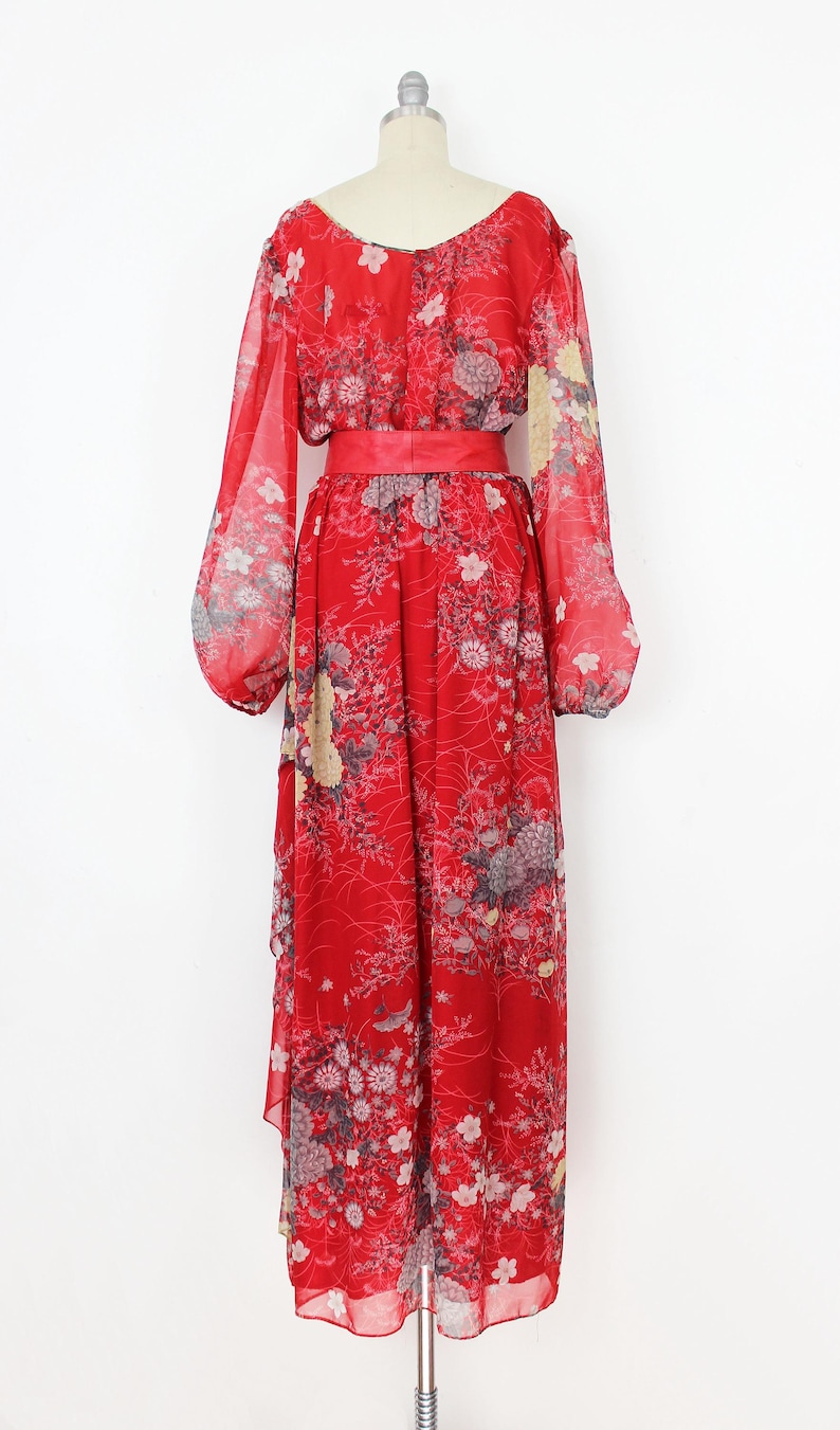 May include: A red maxi dress with a floral print and a matching red sash. The dress has long sleeves and a scoop neckline.