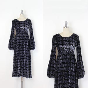 May include: A long, dark gray velvet dress with a repeating skull pattern. The dress features a round neckline, long sleeves with a balloon shape, and a gathered waist. The dress is displayed on a mannequin.