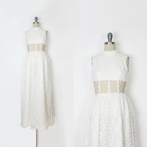 May include: A white lace dress with a high neckline and a sheer panel at the waist. The dress is sleeveless and has a full skirt. The dress is displayed on a mannequin.
