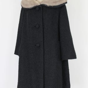 Puede incluir: Un abrigo negro vintage con cuello de piel sint&eacute;tica. El abrigo tiene una tela texturizada, tres botones en la parte delantera y mangas de tres cuartos. El cuello es de color beige claro.
