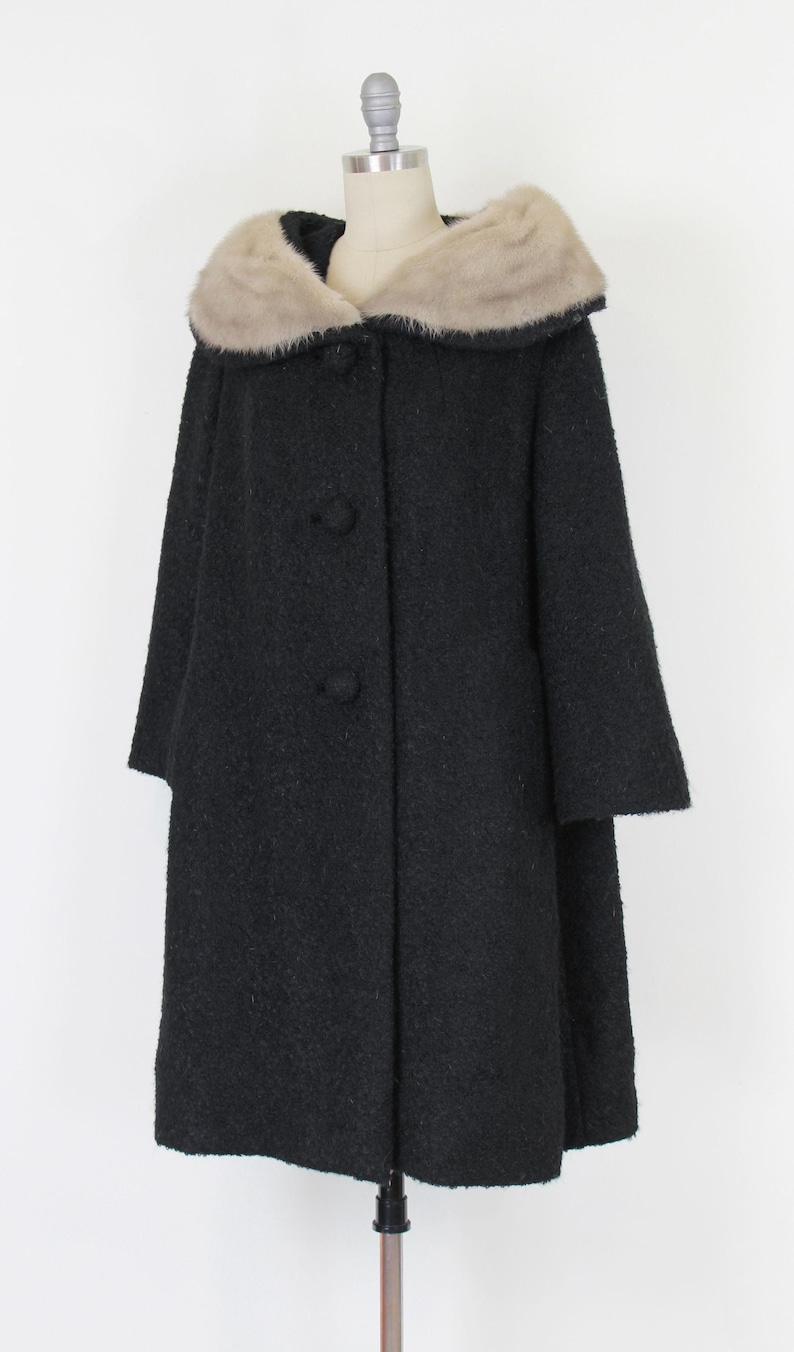 Puede incluir: Un abrigo negro vintage con cuello de piel sint&eacute;tica. El abrigo tiene una tela texturizada, tres botones en la parte delantera y mangas de tres cuartos. El cuello es de color beige claro.