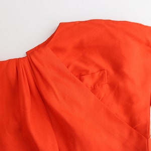 May include: A bright orange top with a gathered neckline and a single pocket on the front.