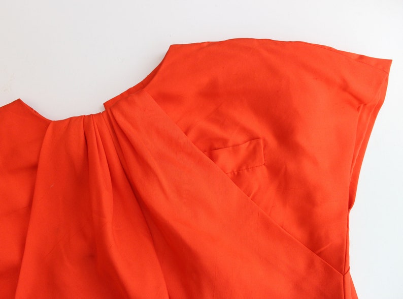 May include: A bright orange top with a gathered neckline and a single pocket on the front.