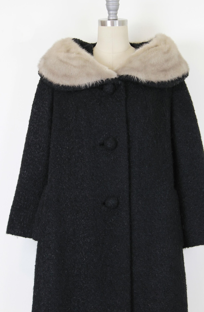 Puede incluir: Un abrigo negro vintage con cuello de piel sint&eacute;tica. El abrigo tiene una tela texturizada y tres botones grandes en la parte delantera. El cuello es de color beige claro, contrastando con el abrigo oscuro.