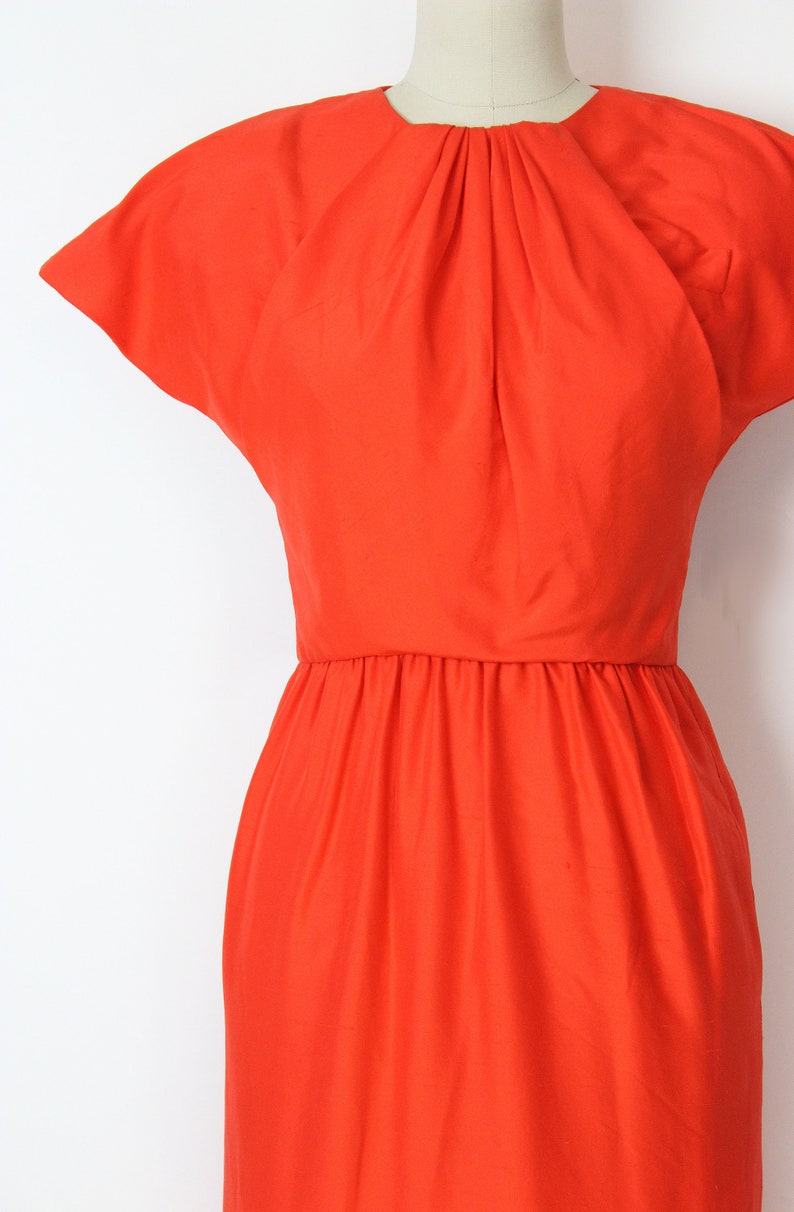 May include: A bright orange dress with a gathered neckline and short, cap sleeves. The dress has a fitted bodice and a flowing skirt.