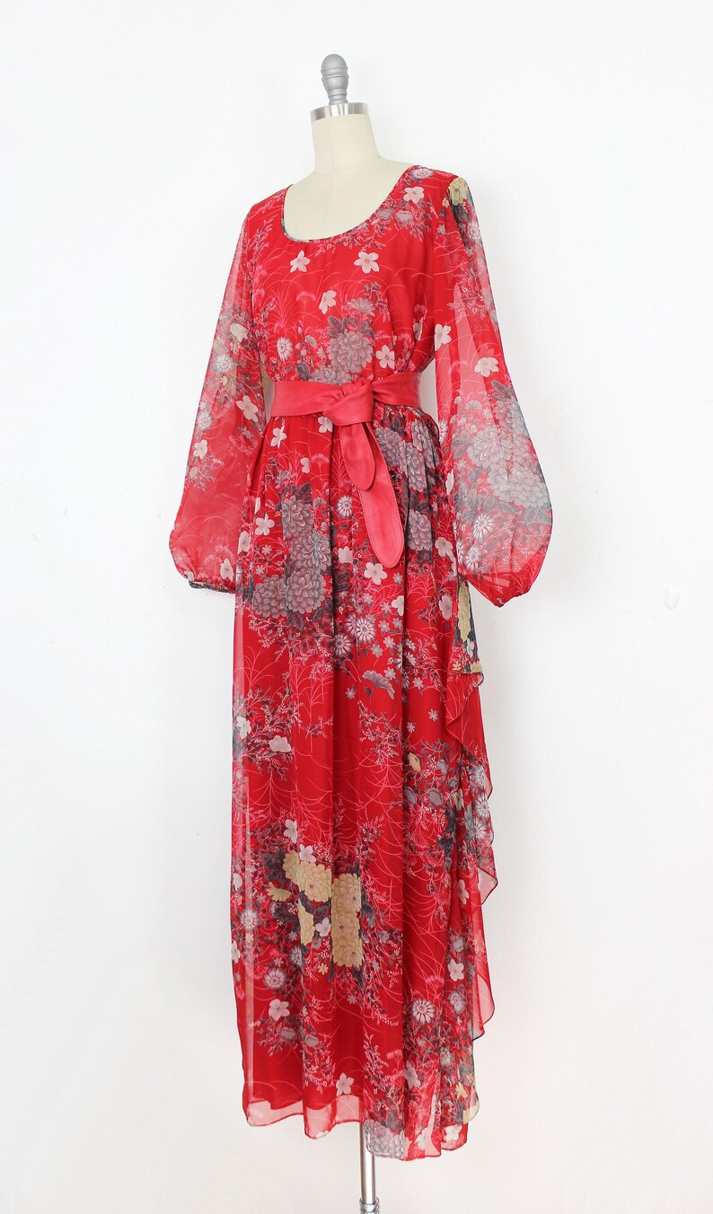 May include: A red maxi dress with a floral print and a matching red sash. The dress has long sleeves and a flowing skirt.