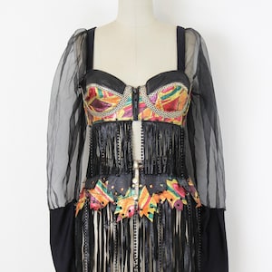 May include: A black and colorful vintage dress with a bustier top and fringe detailing. The top features a colorful geometric pattern and a zipper closure. The dress has long, sheer sleeves and is displayed on a mannequin.