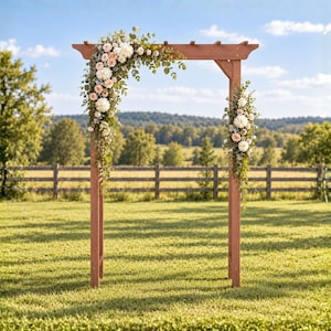 May include: A wooden wedding arch with a reddish-brown finish, decorated with floral arrangements of white and pale pink roses, cream-colored hydrangeas, and green eucalyptus leaves draped across the top left and down the right side post.