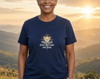 May include: A navy blue short-sleeved t-shirt featuring a graphic of a glowing dove and starburst design with the text "May God Shine His Light on You" printed in white lettering on the center of the chest area.