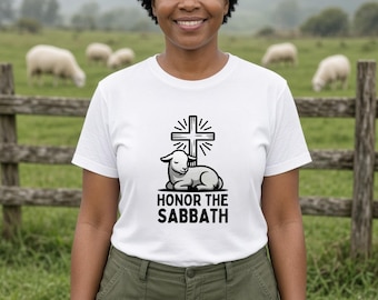May include: A white short-sleeved t-shirt featuring a black graphic of a lamb resting in front of a cross with radiating lines. Below the graphic, the text reads HONOR THE SABBATH in bold, black, sans-serif capital letters.