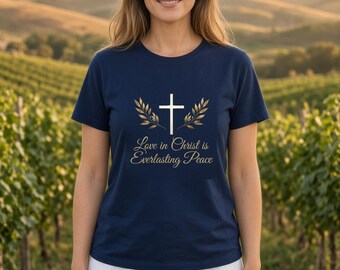 May include: A navy blue short-sleeved t-shirt featuring a white cross graphic flanked by two gold-colored laurel branches. Below the graphic, the text reads, "Love in Christ is Everlasting Peace" in a gold-colored script font.