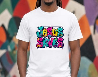 May include: A white short-sleeved t-shirt featuring a central graphic with the text "JESUS SAVES" in a colorful graffiti-style font. The design includes bright blue, pink, and yellow accents with small boombox illustrations.