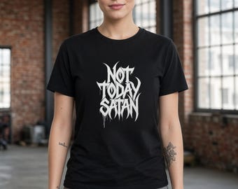May include: A black short-sleeved t-shirt featuring white text that reads "NOT TODAY SATAN" in a stylized, jagged font with a dripping effect. The shirt is paired with grey distressed denim jeans that have visible rips at the knees.