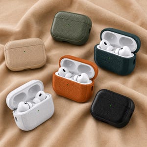Peut inclure: Plusieurs étuis pour AirPods en cuir texturé, de couleurs beige, vert olive, orange, blanc, vert foncé et noir. Certains étuis sont ouverts, révélant des écouteurs blancs. Un petit point vert est visible sur le devant de chaque étui.