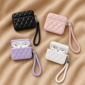 Peut inclure: Quatre étuis pour AirPods matelassés, noirs, roses, lilas et blancs. Chaque étui présente un motif en losange et une dragonne assortie. L'étui lilas est ouvert, révélant des écouteurs blancs.