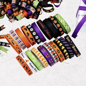 Könnte beinhalten: Eine Auswahl an Halloween-Bändern in Orange, Schwarz, Lila und Grün. Die Bänder sind mit Kürbis-, Totenkopf- und Spinnennetzmustern sowie den Wörtern "Boo!" und "Happy Halloween" verziert.