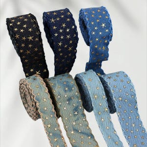 May include: Several rolls of decorative ribbon in various shades of blue and black. Each ribbon is adorned with gold star patterns. The edges of some ribbons have a scalloped trim. The ribbons are ideal for crafting and gift wrapping.