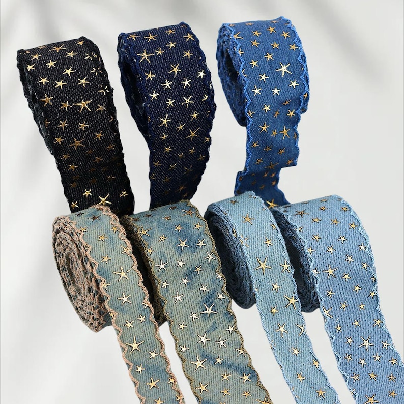 May include: Several rolls of decorative ribbon in various shades of blue and black. Each ribbon is adorned with gold star patterns. The edges of some ribbons have a scalloped trim. The ribbons are ideal for crafting and gift wrapping.