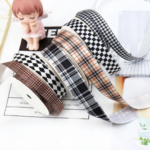 Könnte beinhalten: Eine Sammlung von Stoffbändern auf Spulen mit verschiedenen Mustern, darunter schwarz-weißes Hahnentrittmuster, schwarz-weißes Schachbrettmuster, beige-schwarzes Plaid, schwarz-weißes Schottenmuster und ein braunes Rautenmuster mit kleinen weißen Sternen.