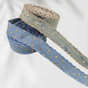 May include: Two spools of decorative ribbon. One is blue with gold star accents and a scalloped edge. The other is a muted green with gold star accents and a scalloped edge. The ribbon is made of a denim-like material.