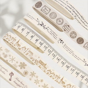 Peut inclure: Plusieurs rouleaux de ruban décoratif blanc cassé sont présentés. Certains rubans présentent un motif de règle avec des mesures en centimètres, tandis que d'autres ont des motifs imprimés de maisons, de flocons de neige et d'éléments botaniques.