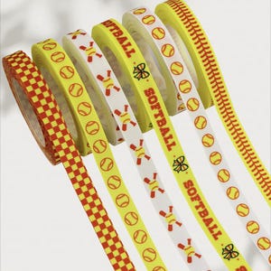 Pode incluir: Uma coleção de fitas com tema de softball em vários designs. As fitas apresentam padrões de bolas de softball, costuras de beisebol e a palavra "SOFTBALL". As cores incluem amarelo, vermelho e branco. As fitas estão em rolos.