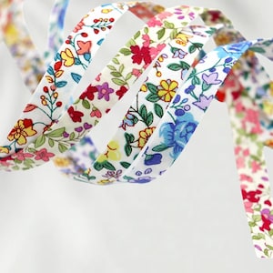 Könnte beinhalten: Nahaufnahme von floral gemusterten Bändern in verschiedenen Farben. Die Bänder haben einen weißen Hintergrund mit bunten Blumen und grünen Blättern. Die Bänder sind gewellt und verdreht, wodurch ein dynamischer und dekorativer Effekt entsteht. Ideal für Bastelarbeiten und Verzierungen.