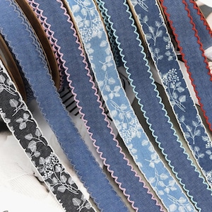 May include: Selection of decorative ribbons in shades of blue and black, featuring white floral designs and scalloped edges. Some ribbons have pink or red stitching. Suitable for crafts and embellishments.