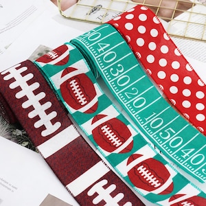 Könnte beinhalten: Drei Rollen Drahtband mit Sportmotiven. Eine Rolle ist dunkelrot mit weißen Football-Schnürsenkeln, eine ist grün mit Footballs und Spielfeldmarkierungen und eine ist hellrot mit einem weißen Punktemuster auf einer Stofftextur.