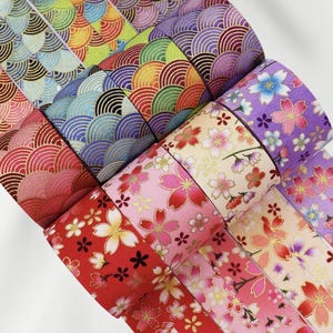 Könnte beinhalten: Eine Sammlung dekorativer Washi-Tape-Rollen mit verschiedenen japanisch inspirierten Mustern. Die Designs umfassen farbenfrohe Wellenmuster und florale Motive in Rot-, Rosa-, Lila- und Goldtönen. Ideal für Bastelarbeiten und Scrapbooking.