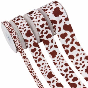 Peut inclure: Quatre bobines de ruban gros-grain avec un motif répétitif de taches de vache marron et blanc. Les rubans sont disposés en rangée, montrant des largeurs variables, chacun avec une surface texturée et un motif tacheté cohérent.