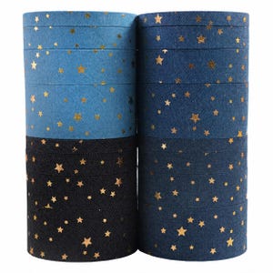Könnte beinhalten: Zwei Stapel von Stoffbandrollen mit einer jeansartigen Textur in den Farben Hellblau, Mittelblau und Schwarz. Jede Rolle ist mit einem sich wiederholenden Muster aus kleinen, metallisch goldenen Sternen auf der Oberfläche verziert.