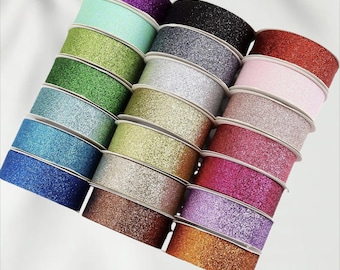 May include: A collection of glitter ribbon rolls in various colors, including purple, green, blue, silver, gold, pink, and red. Each roll is approximately 10 yards in length. The ribbon has a shiny, textured surface.