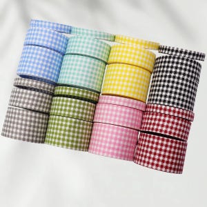 Könnte beinhalten: Eine Sammlung von gerollten Vichy-Karobändern in verschiedenen Farben, darunter Blau, Grün, Gelb, Schwarz, Rot, Rosa und Grau. Die Bänder zeigen ein klassisches Karomuster, ideal für Bastelarbeiten und Dekorationen.