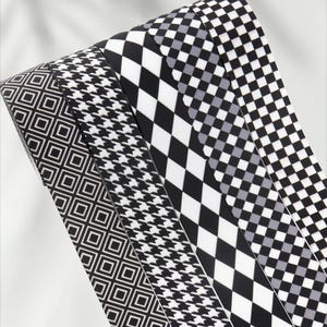 Könnte beinhalten: Nahaufnahme von Bändern mit schwarz-weißem Muster. Zu den Designs gehören geometrische Quadrate, Hahnentrittmuster und Rautenmuster. Die Bänder sind aufgerollt und zeigen die verschiedenen Muster für Bastelarbeiten und Dekorationen.